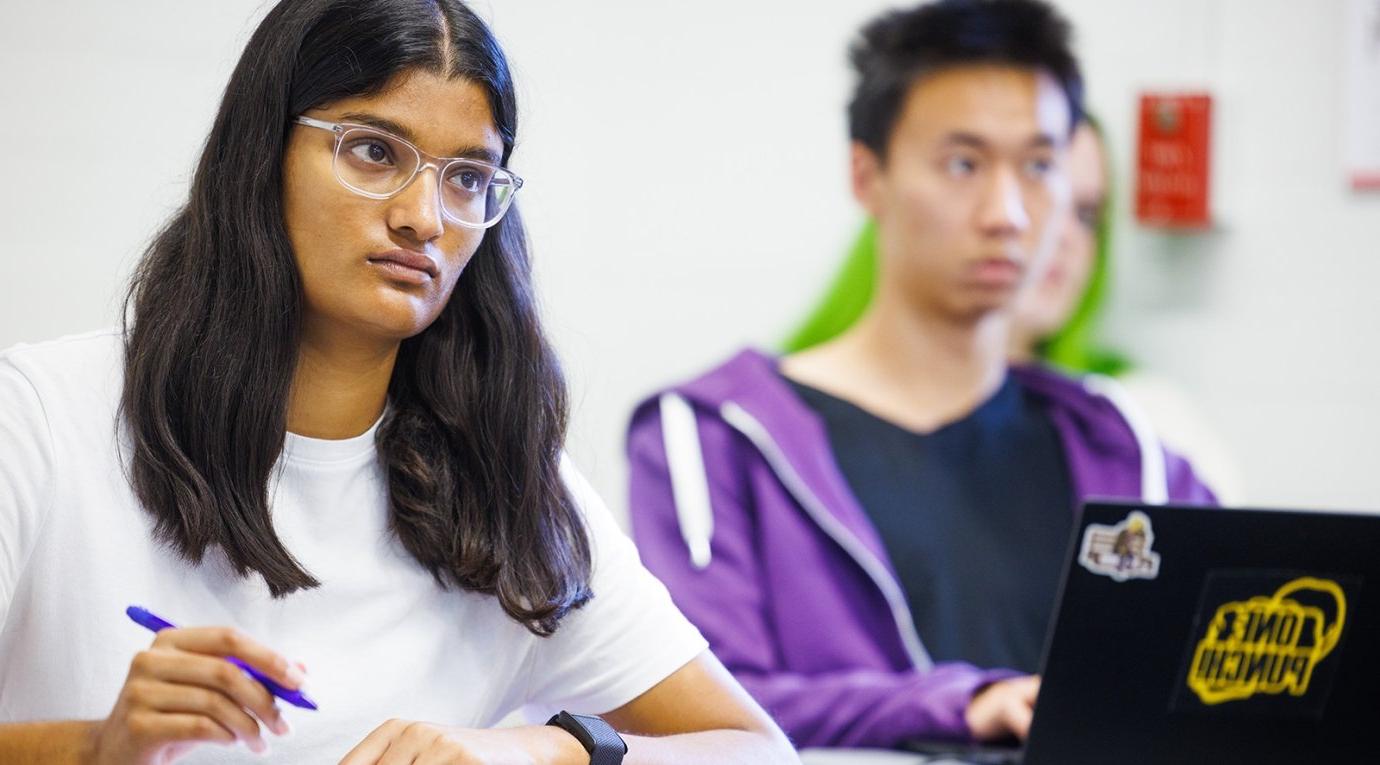 Two students take notes during a class lecture. 