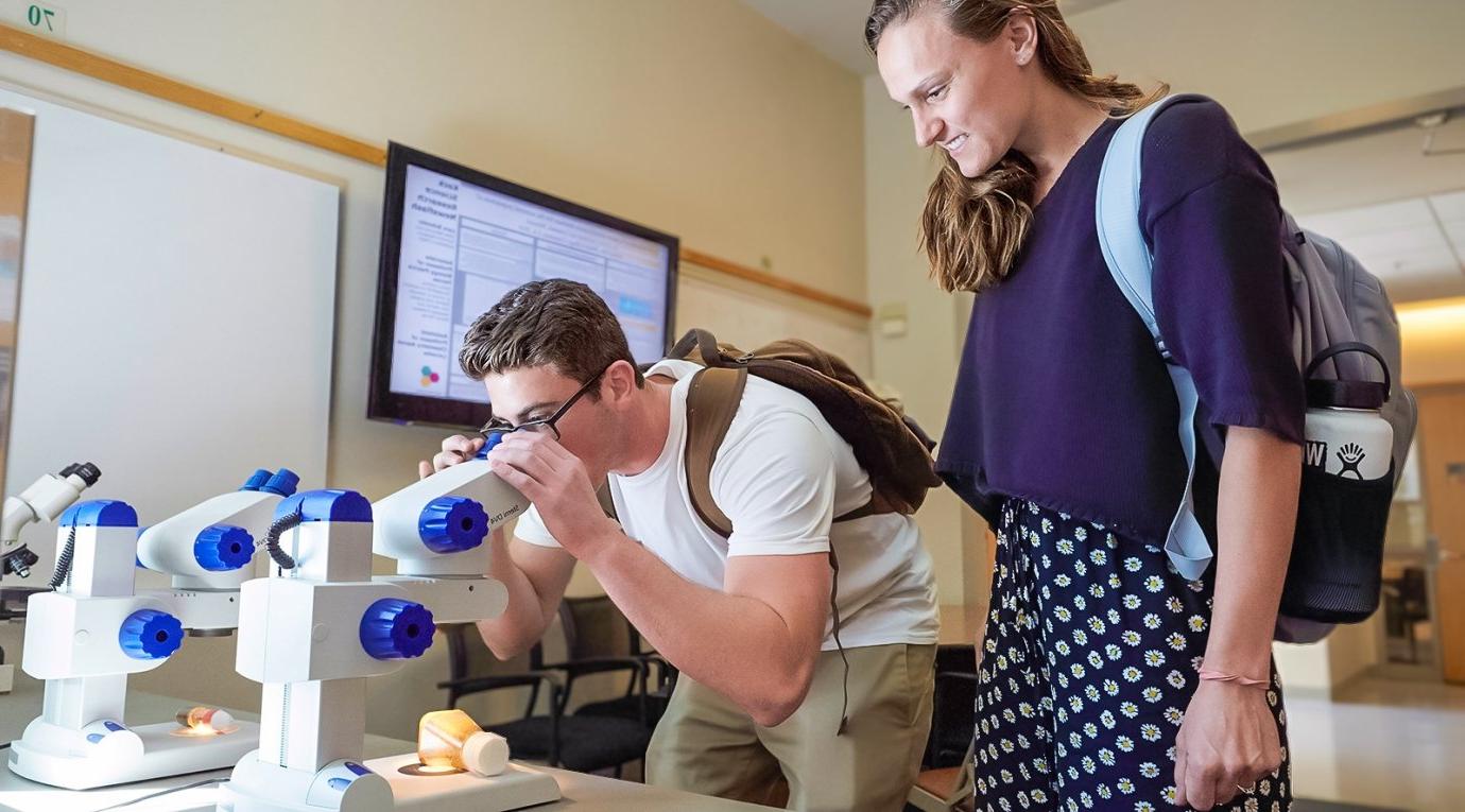 a student peers into a microscope while his classmate looks on