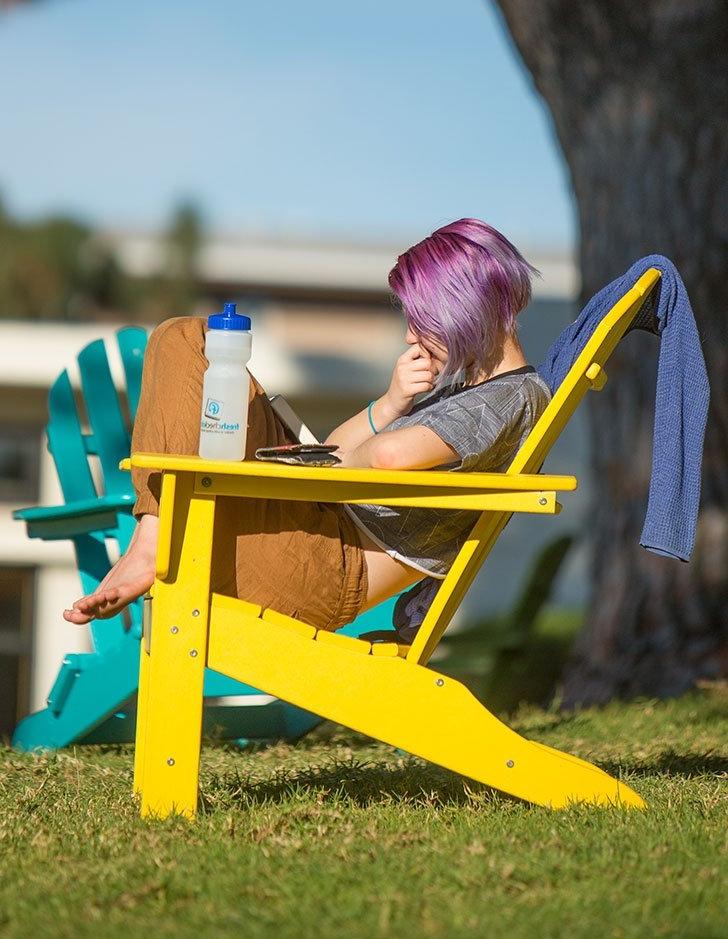 a student with puruple hair sits in a yellow adirondack chair on the mounds and reads