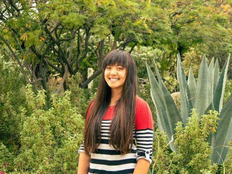 Shelby Ottengheime wears a red, blck, and white striped sweater while standing in front of succulents.